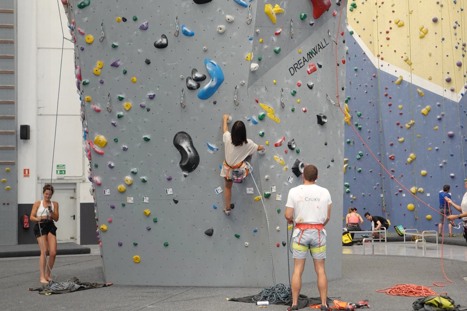 Escaladora en vía de rocódromo con su asegurador desde el suelo